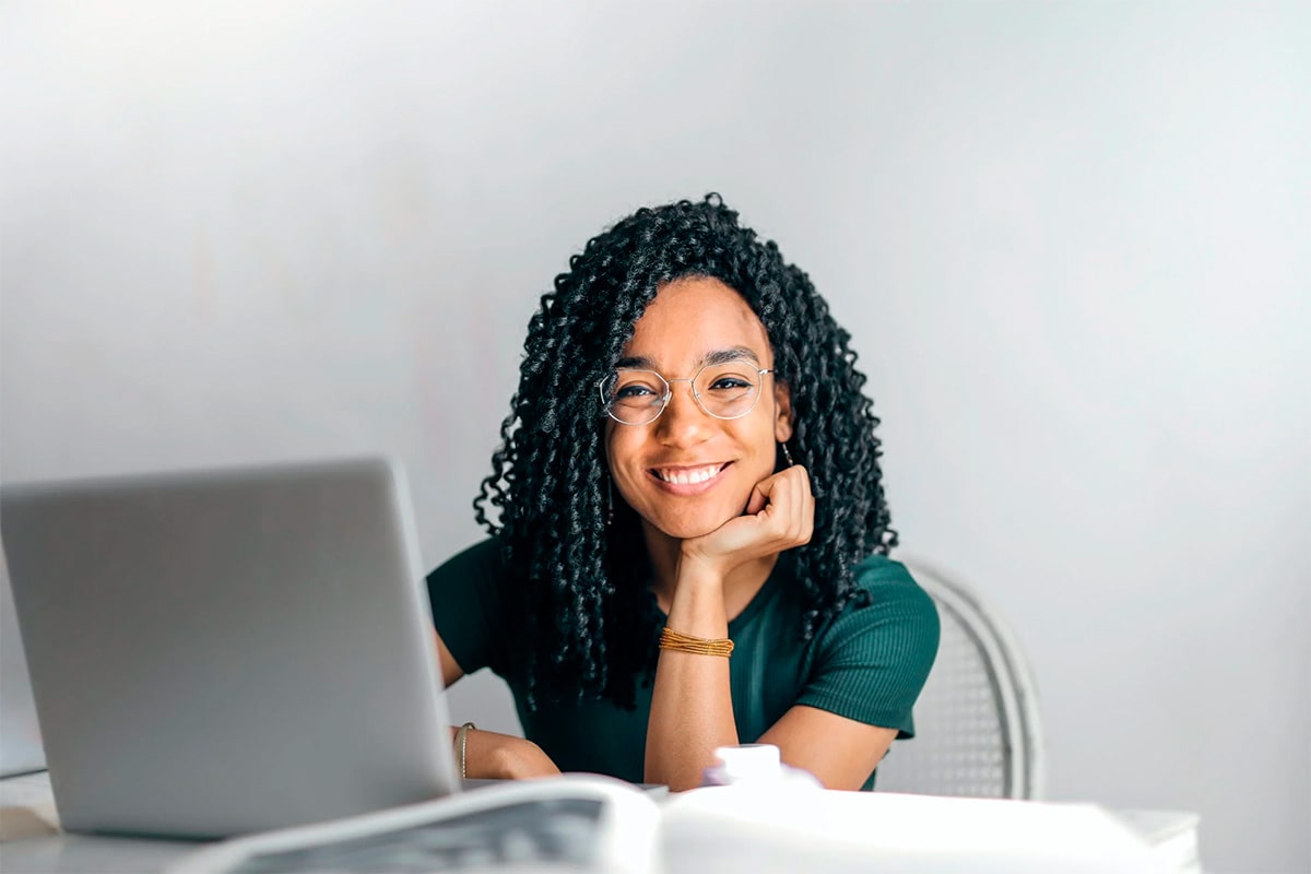 Happy ethnic woman sitting at table with laptop